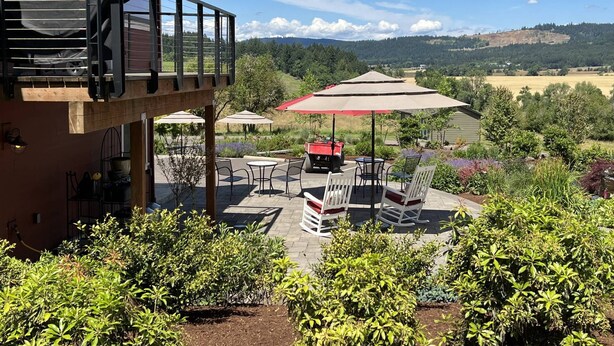 Un patio con mobiliario exterior, una zona de parrillada cubierta y vistas a un paisaje montañoso.