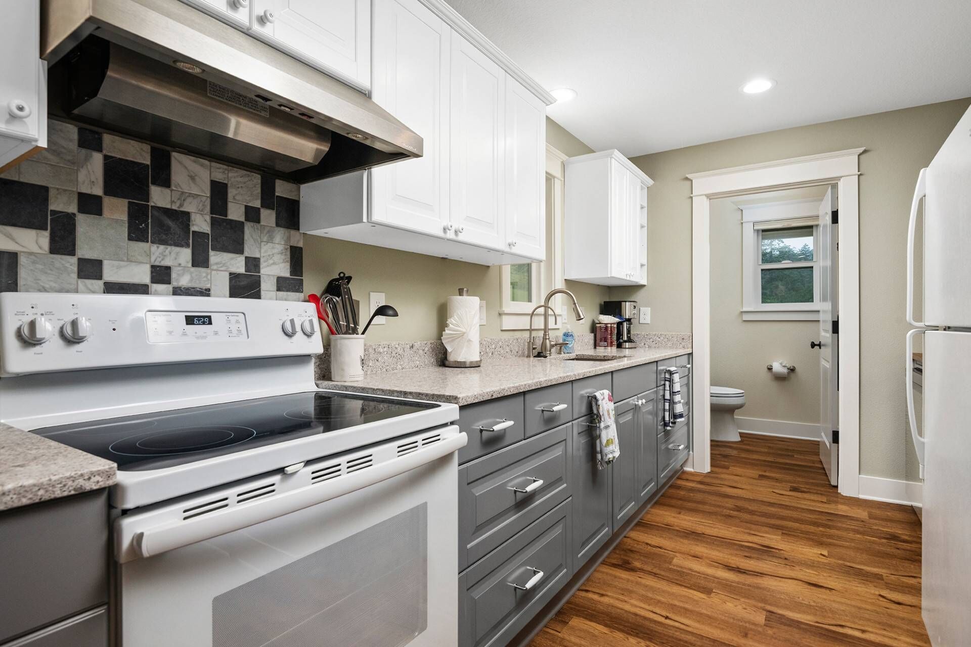 A modern kitchen with white cabinets, a black and white tiled backsplash, a stainless steel range hood, and a built-in oven.
