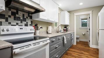 A modern kitchen with white cabinets, a black and white tiled backsplash, a stainless steel range hood, and a built-in oven.