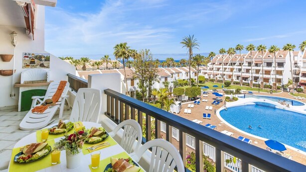 A balcony with a dining table set for two, overlooking a swimming pool and a resort building. - 231 Parque Santiago II, 2 bedrooms, 2 bathrooms, Wi-Fi, beach and pool (Arona)