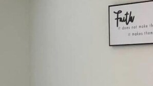 A bedroom with a bed, a bedside lamp, and a wall with a motivational quote.