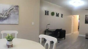 A dining area with a white table and chairs, a small potted plant, and a wall-mounted sign that reads "HOME".