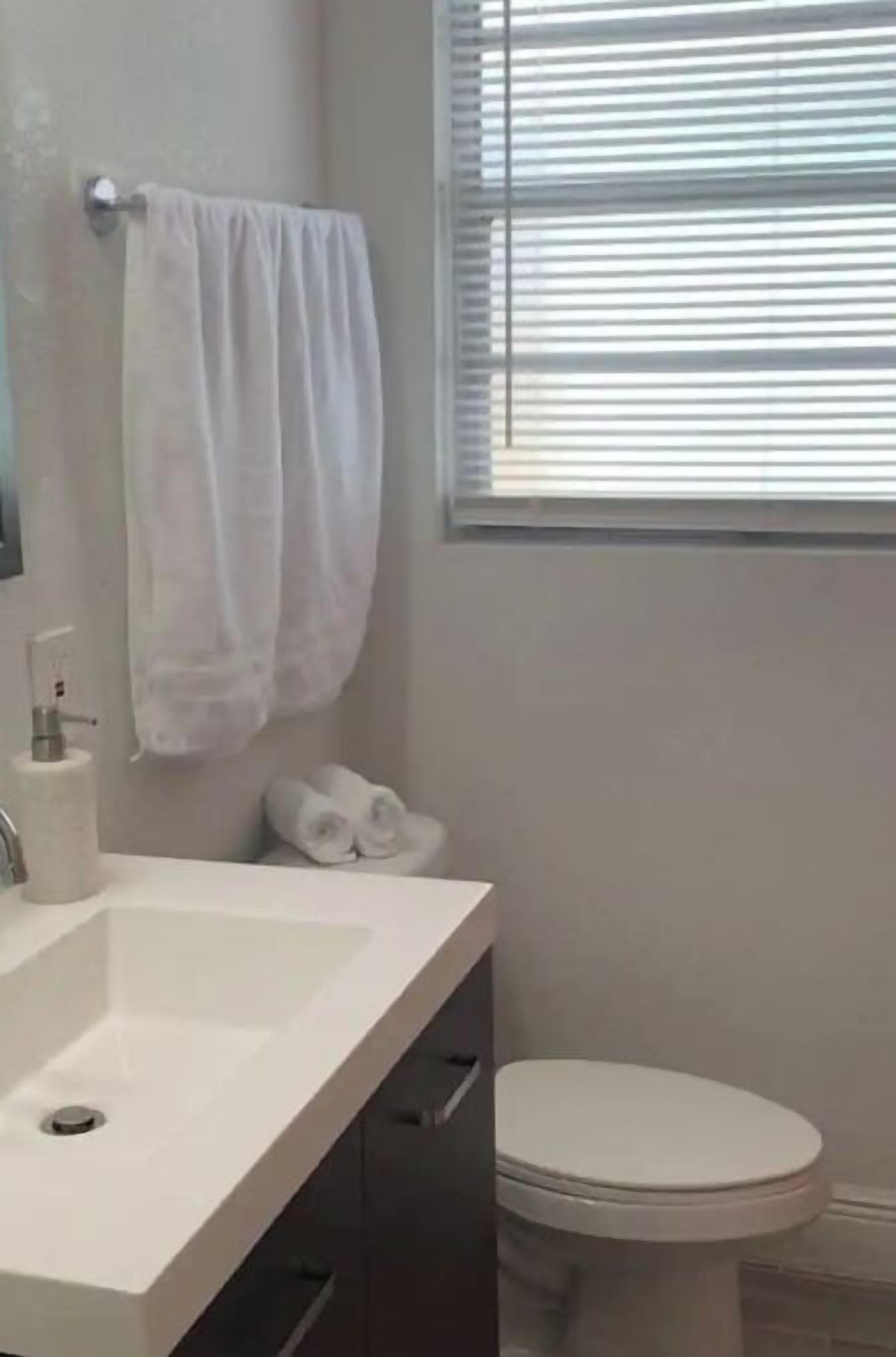 A bathroom with a white sink, a toilet, and a window with blinds.