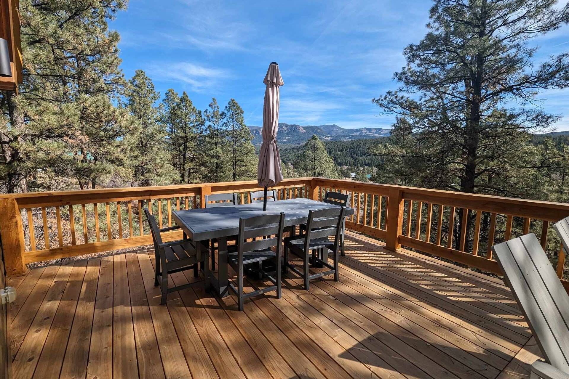 Une terrasse en bois avec une table et des chaises, offrant une vue sur une forêt et des montagnes.