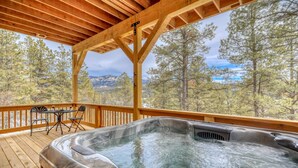 Eine Holzterrasse mit Whirlpool, Tisch und Stühlen sowie Blick auf das Gebirge.