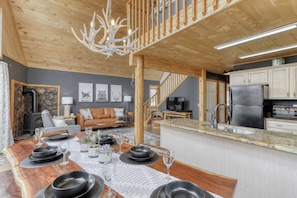 Uma cozinha moderna com ilha integrada, uma sala de jantar com mesa de madeira para seis pessoas e um espaço de estar acolhedor com lareira.