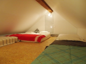 A small, cozy attic bedroom with two beds, a wooden ceiling beam, and a single light fixture.