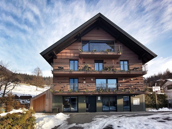 A multi-story hotel with balconies, a wooden facade, and a snow-covered ground.