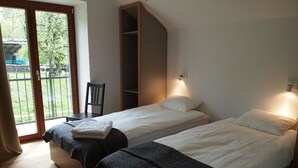 A room with two beds, a chair, a wardrobe, and a sliding glass door to the outside.