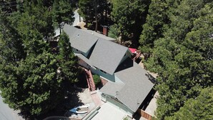 Vue aérienne d’une maison à toit en pente, entourée d’arbres denses.