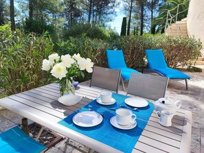A table set outdoors with chairs, a vase of white flowers, and a view of trees and a building in the background. - 2 apartments in a beautiful, quiet complex nestled between vineyards and the sea. Large Swimming Pool (LES ARCS)