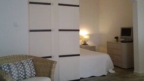 A bedroom with a bed, a nightstand, a lamp, a TV, and a chair with a patterned cushion. - 2 apartments in a beautiful, quiet property between vineyards and the sea. Large swimming pool (LES ARCS)