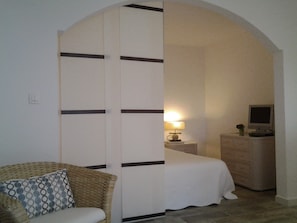 A bedroom with a bed, a nightstand, a lamp, a TV, and a chair with a patterned cushion.