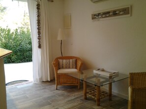 A room with a wicker chair, a glass-top table, and a wall-mounted lamp.