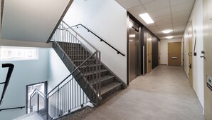 A modern hotel corridor with a staircase, elevator, and doors leading to rooms. - Hiisi Homes Hämeenlinna Asemanranta (Hameenlinna)