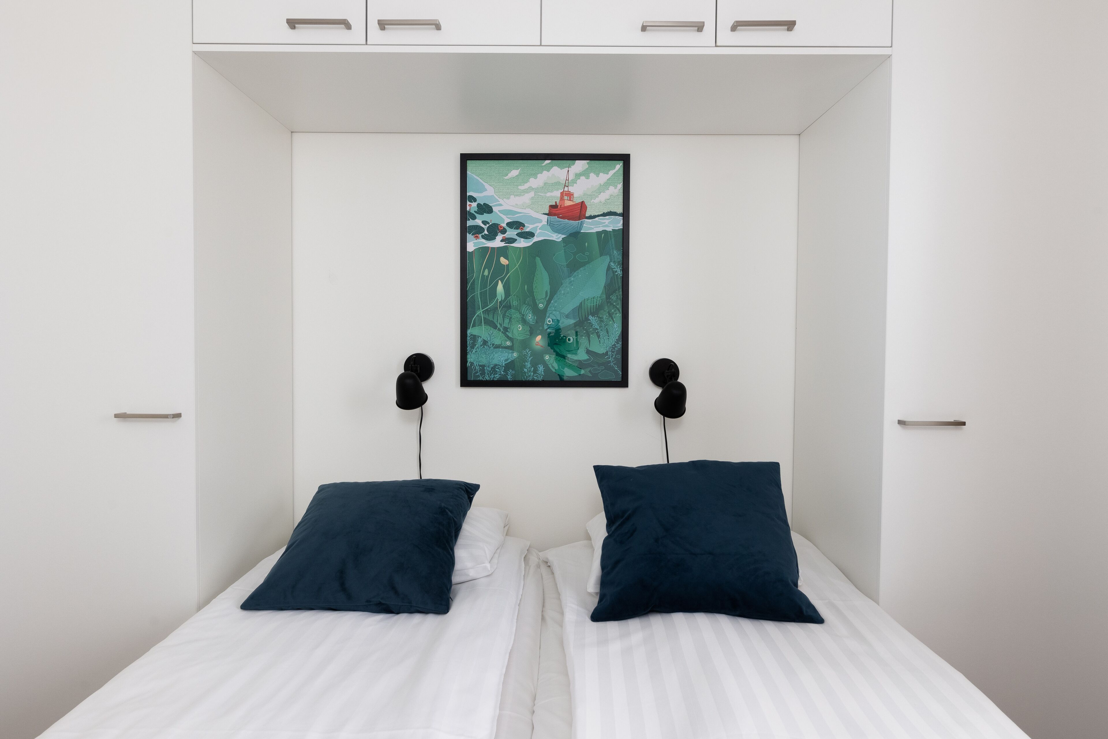 A bedroom with a bed, two pillows, a framed picture on the wall, and a white wardrobe.