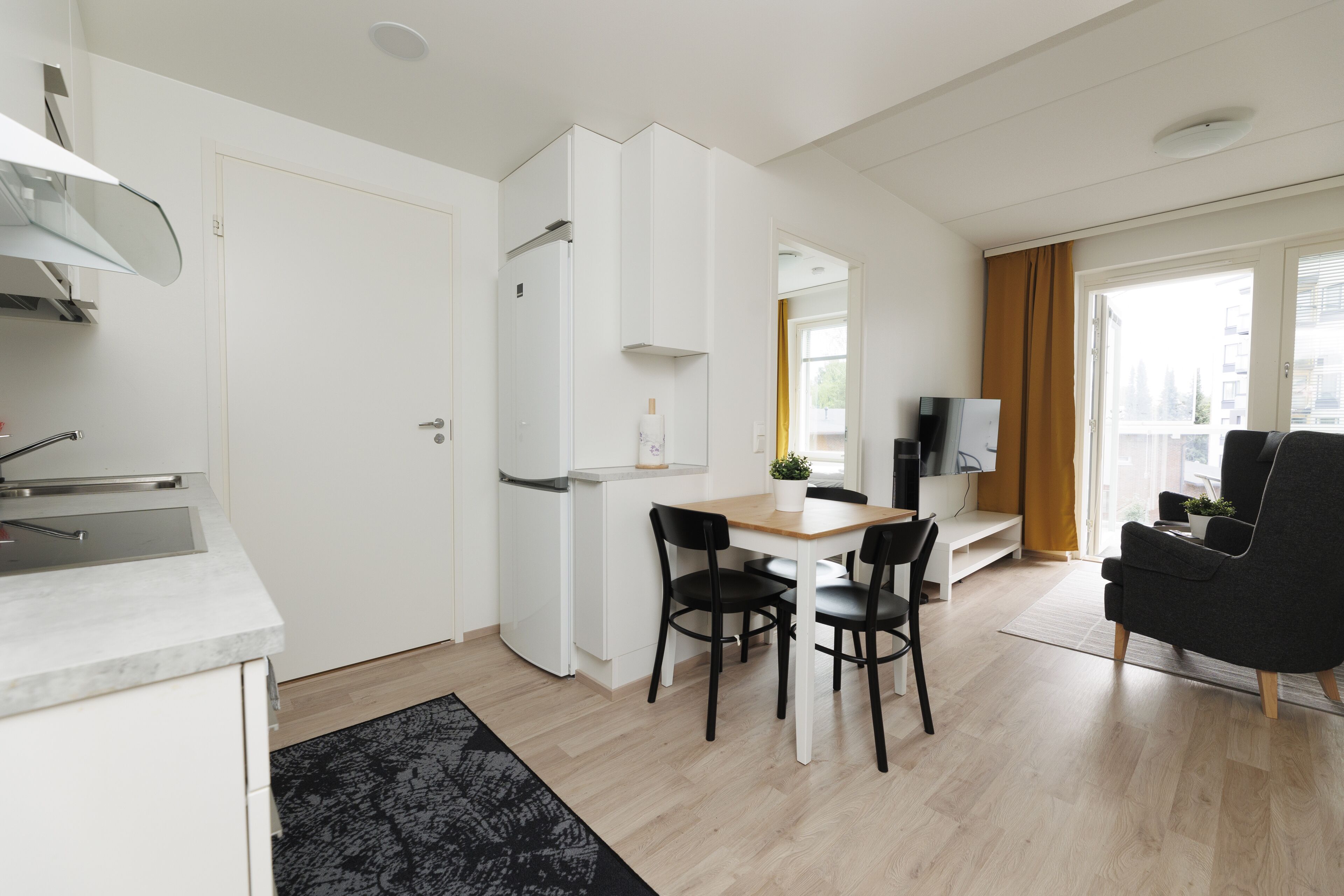 Eine moderne Küche mit weißen Schränken, einem eingebauten Backofen und einem Essbereich mit Holztisch und schwarzen Stühlen.