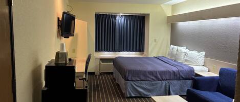 Una habitación de hotel con cama, escritorio, silla, televisor y ventana con cortinas.