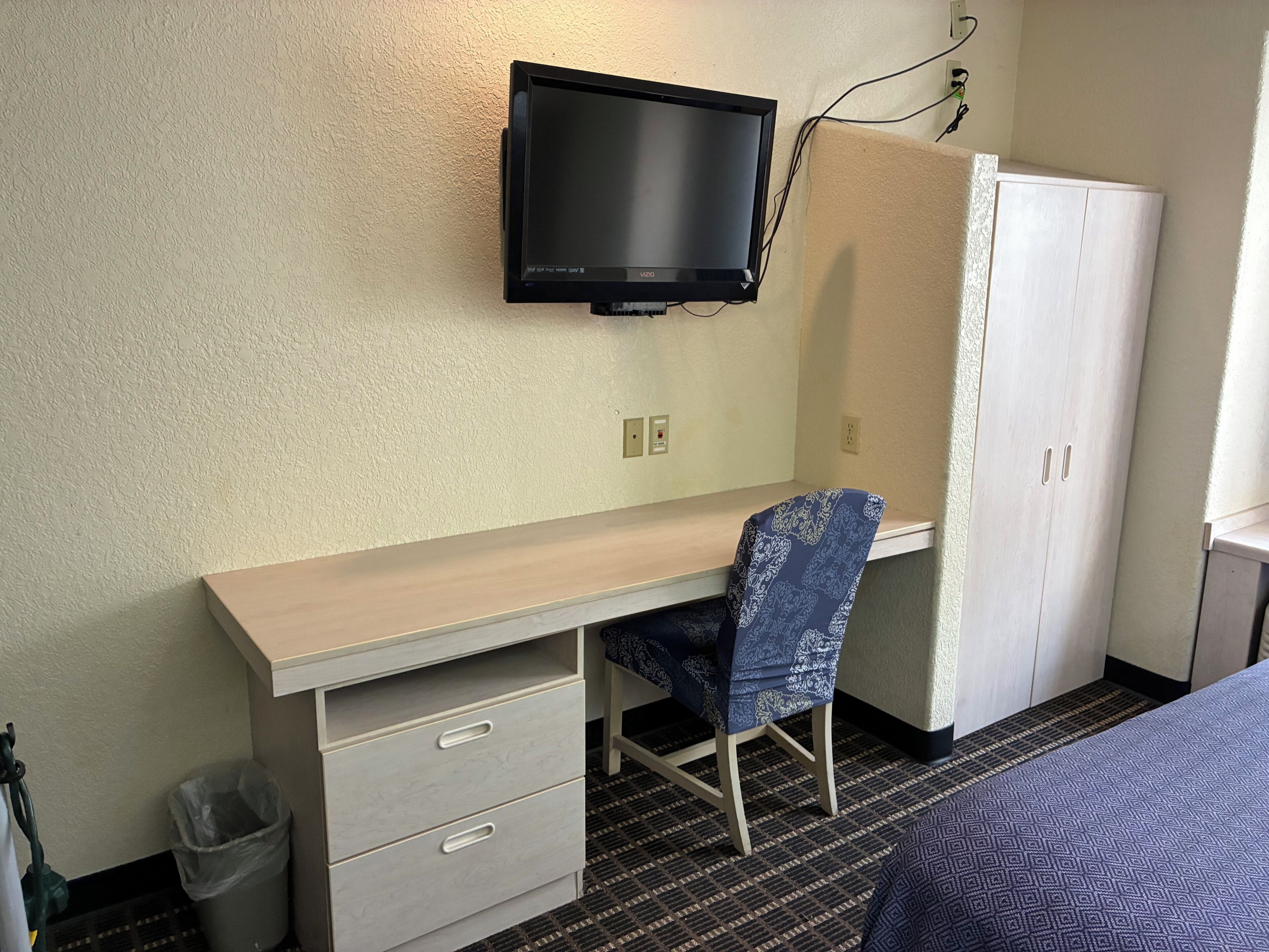 Habitación de hotel con escritorio, silla, televisor, armario y cama.