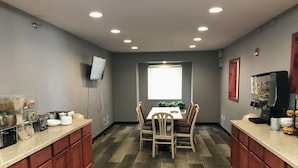 A modern kitchen with wooden cabinets, a dining table with chairs, a coffee machine, and a TV mounted on the wall.
