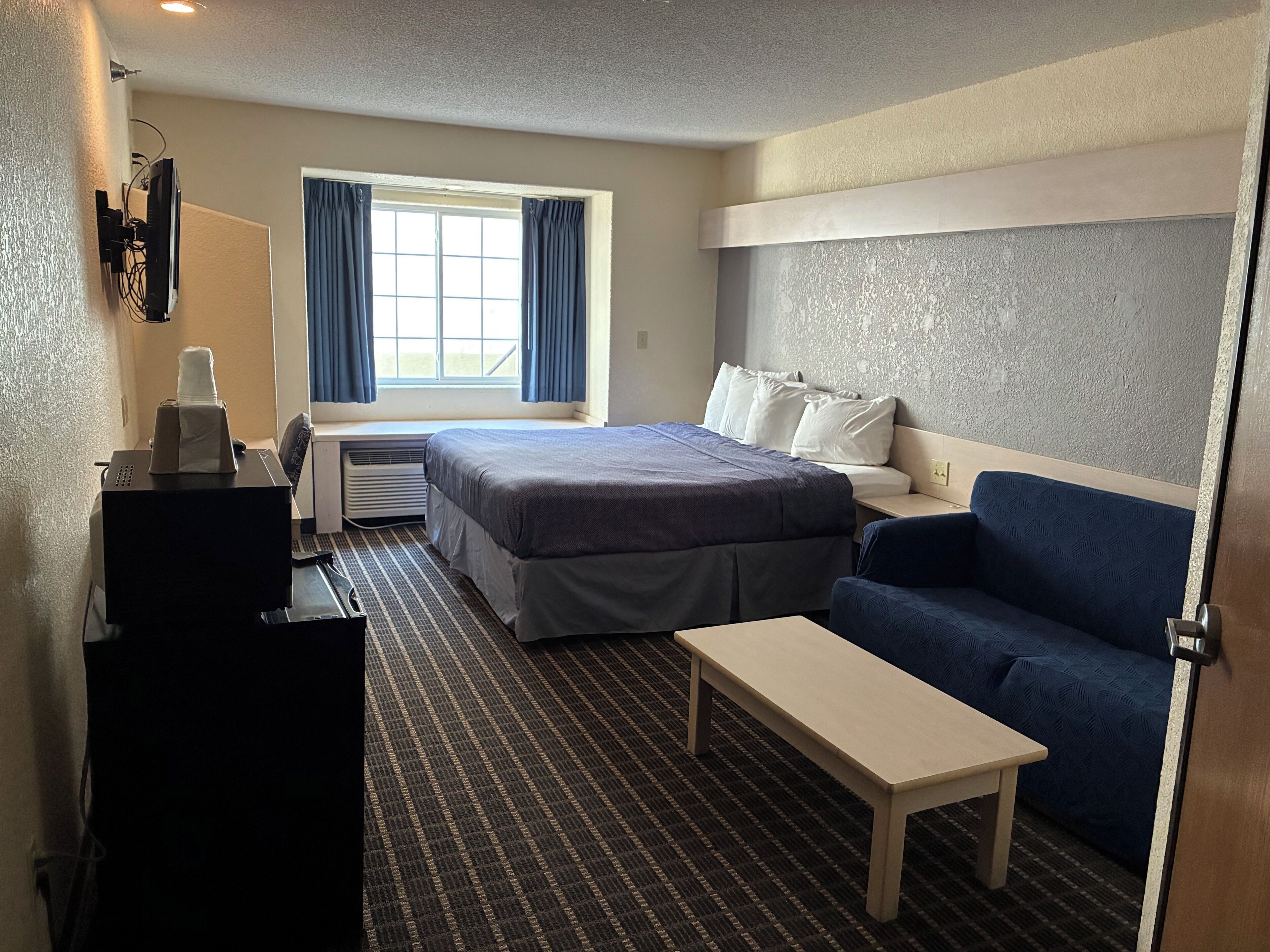 A hotel room with a bed, a sofa, a desk, and a window with curtains.