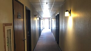 A long, narrow hallway with carpeted floors and walls, featuring doors on both sides and wall-mounted light fixtures.