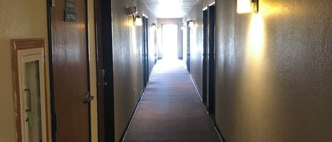Un long couloir étroit, doté de revêtements de sol et de murs en moquette, avec des portes de part et d’autre et des luminaires fixés au mur.
