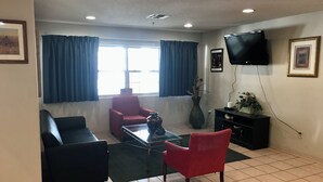 A living room with a red armchair, a black sofa, a glass coffee table, and a TV mounted on the wall.