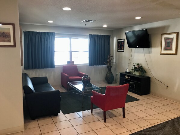A living room with a red armchair, a black sofa, a glass coffee table, and a TV mounted on the wall. - Chadron Inn & Suites (Chadron)