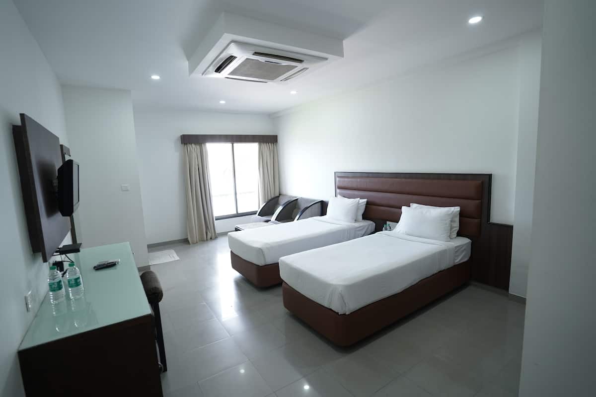 Habitación de hotel con dos camas, un escritorio con silla, televisor de pantalla plana y ventana con cortinas.
