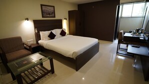 A hotel room with a bed, a desk, a chair, a glass coffee table, and a wall-mounted TV. - Metropolis Hotel (Hubli)