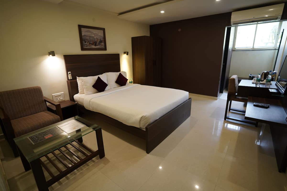 Habitación de hotel con cama, escritorio, silla, mesa de centro de vidrio y televisor montado en la pared.