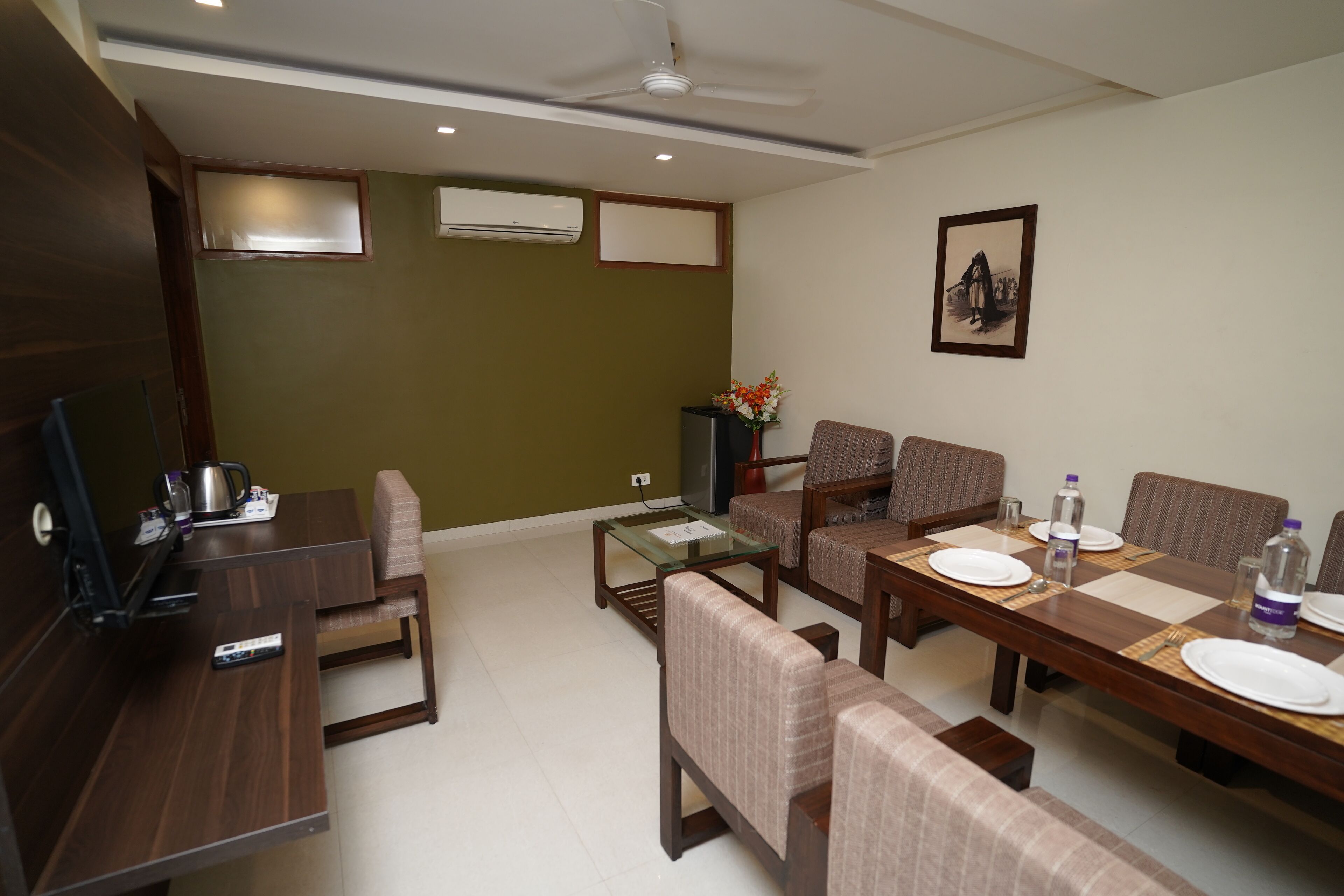 A dining area with a long wooden table, cushioned chairs, a television, and a ceiling fan.