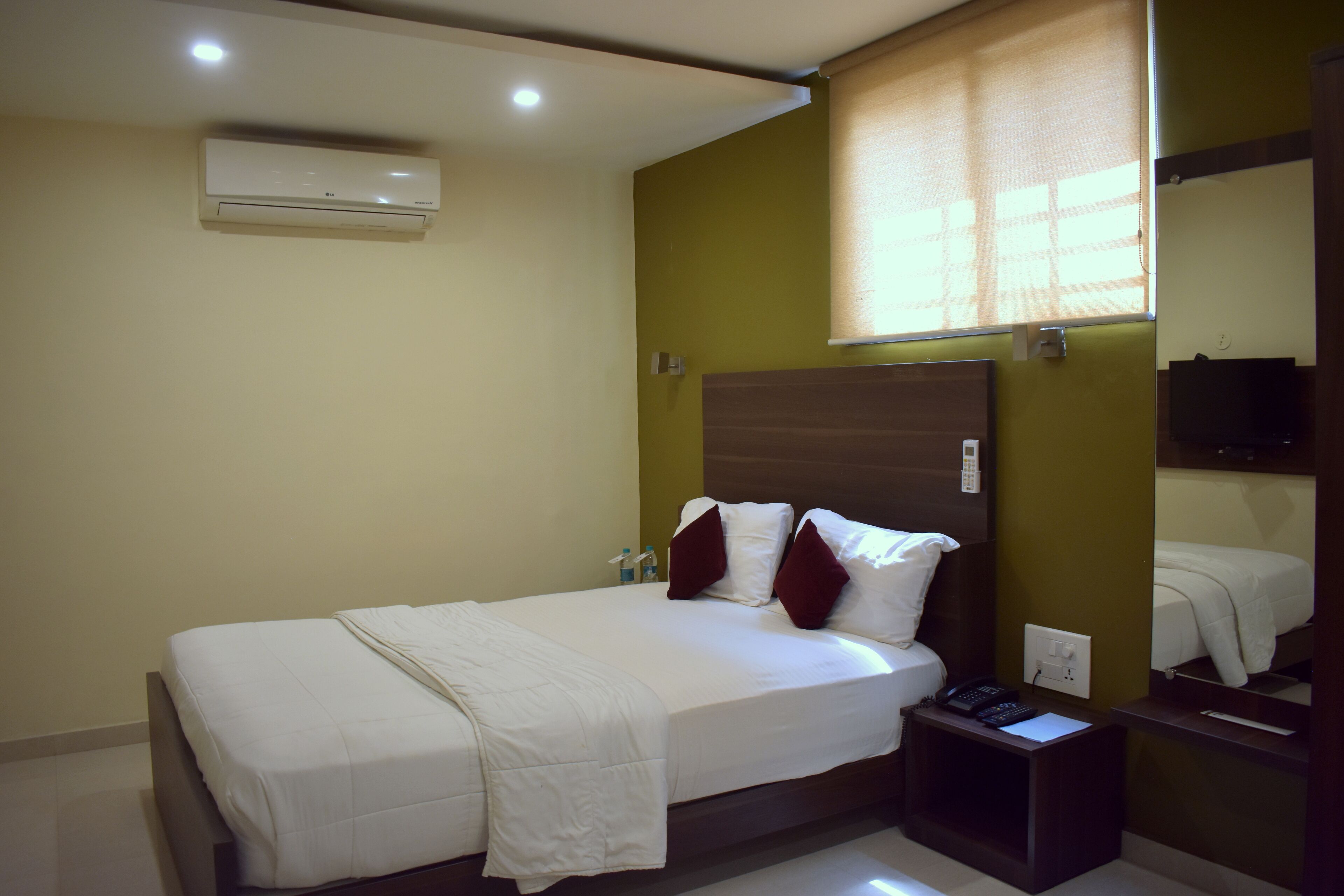 A hotel room with a bed, bedside table, and a mirror.