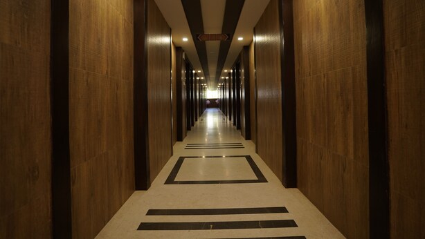 A long, narrow hallway with wooden walls and a patterned floor, leading to a bright area at the end. - Metropolis Hotel (Hubli)