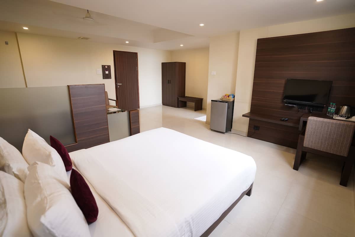 Habitación de hotel con una cama grande, un escritorio con televisor, armario y un refrigerador pequeño.
