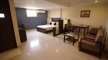 A hotel room with a bed, a desk, a chair, a small table, and a sofa.