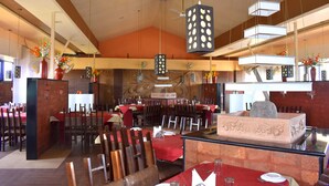 A restaurant with multiple tables and chairs, a central island with a stone countertop, and hanging pendant lights. - Metropolis Hotel (Hubli)
