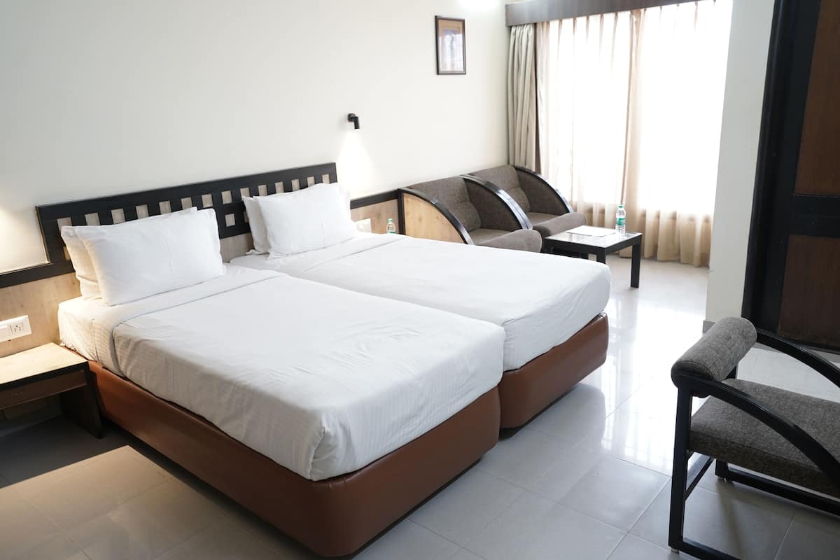 Habitación de hotel con dos camas, un escritorio, una silla y una ventana con cortinas.