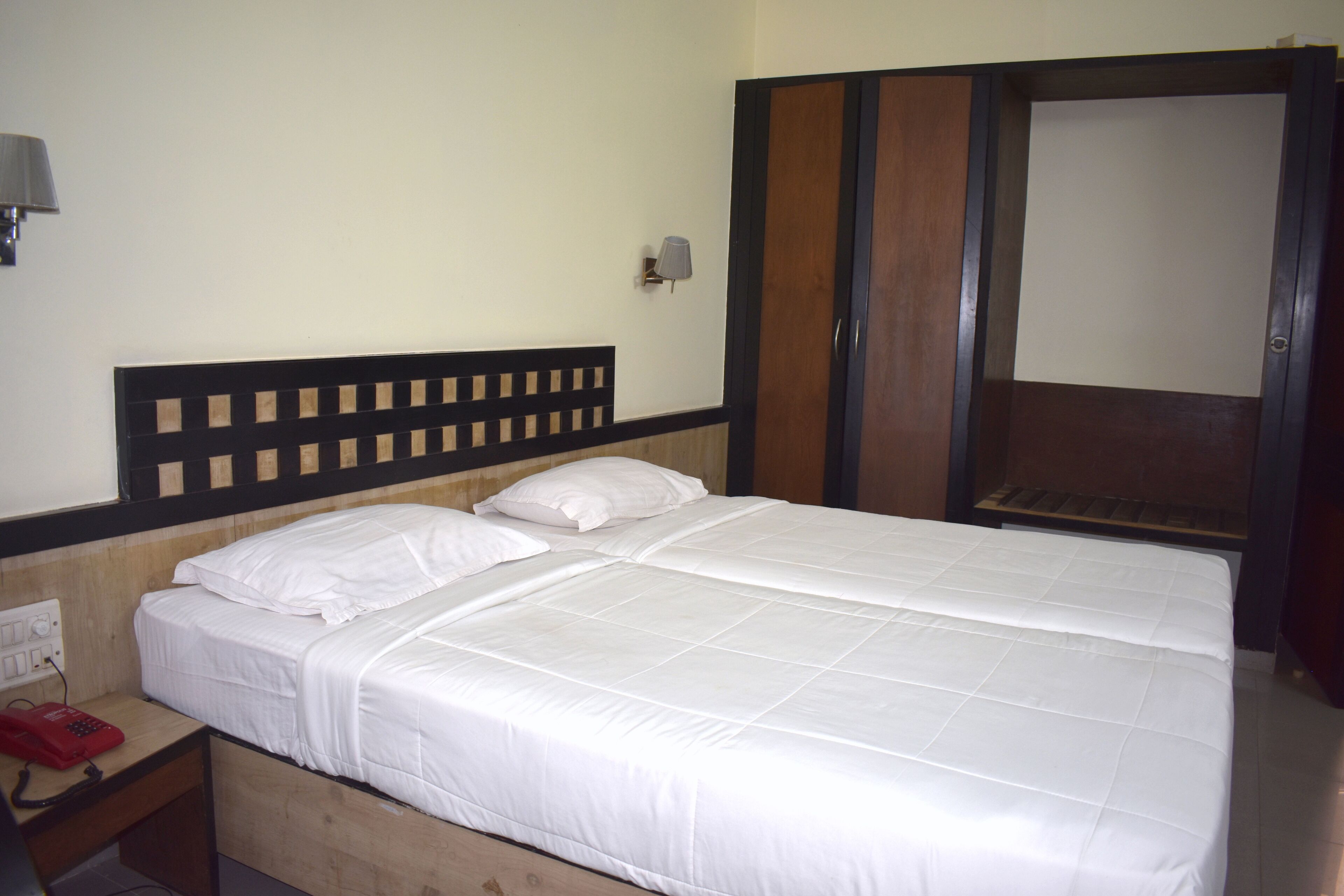 A double bed with white bedding, a wooden headboard, a bedside table with a lamp, and a wardrobe with a mirror.