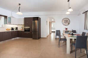 A modern kitchen with dark cabinets, a stainless steel refrigerator, and a dining area with a table and chairs.