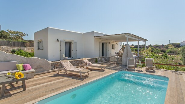 A poolside area with a pool, lounge chairs, a covered seating area, and a stone wall. - SEASIDE VILLA MARIA (PAROS)