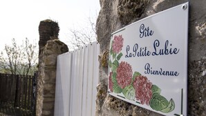 Un letrero de bienvenida con ilustraciones florales y texto en un idioma extranjero, sujeto a una pared de piedra.