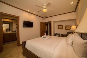 Une chambre d’hôtel avec un lit, un ventilateur de plafond, un téléviseur fixé au mur et un bureau avec une lampe.