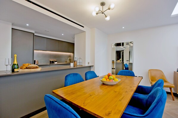 A modern dining area with a wooden table, blue upholstered chairs, and a fruit bowl.