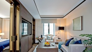 Ein modernes Hotelzimmer mit einem großen Bett, einer Couch, einem Couchtisch mit Früchten, einem Fernseher und Blick auf die Stadt.