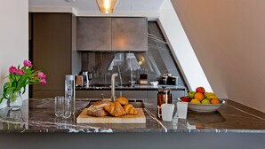 Eine moderne Küche mit Marmorarbeitsplatte, einem Holzbruchbrett mit Croissants, einer Obstschale und einem Blumenstrauß.
