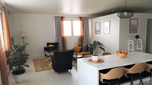Ein modernes Wohnzimmer mit einer Couch, einem Esstisch mit Stühlen, einer Topfpflanze und einem kleinen Tisch mit einer Fruchtschale.
