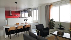 Ein modernes Wohnzimmer mit grauem Sofa, einem Esstisch mit Stühlen und einer Küchenzeile mit roter Spritzschutzwand.