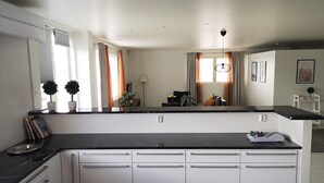 A modern kitchen with white cabinets, black countertops, and a central island. There are potted plants on the windowsill and a lamp on the island. - The HOME of Hiisi (Vihti)
